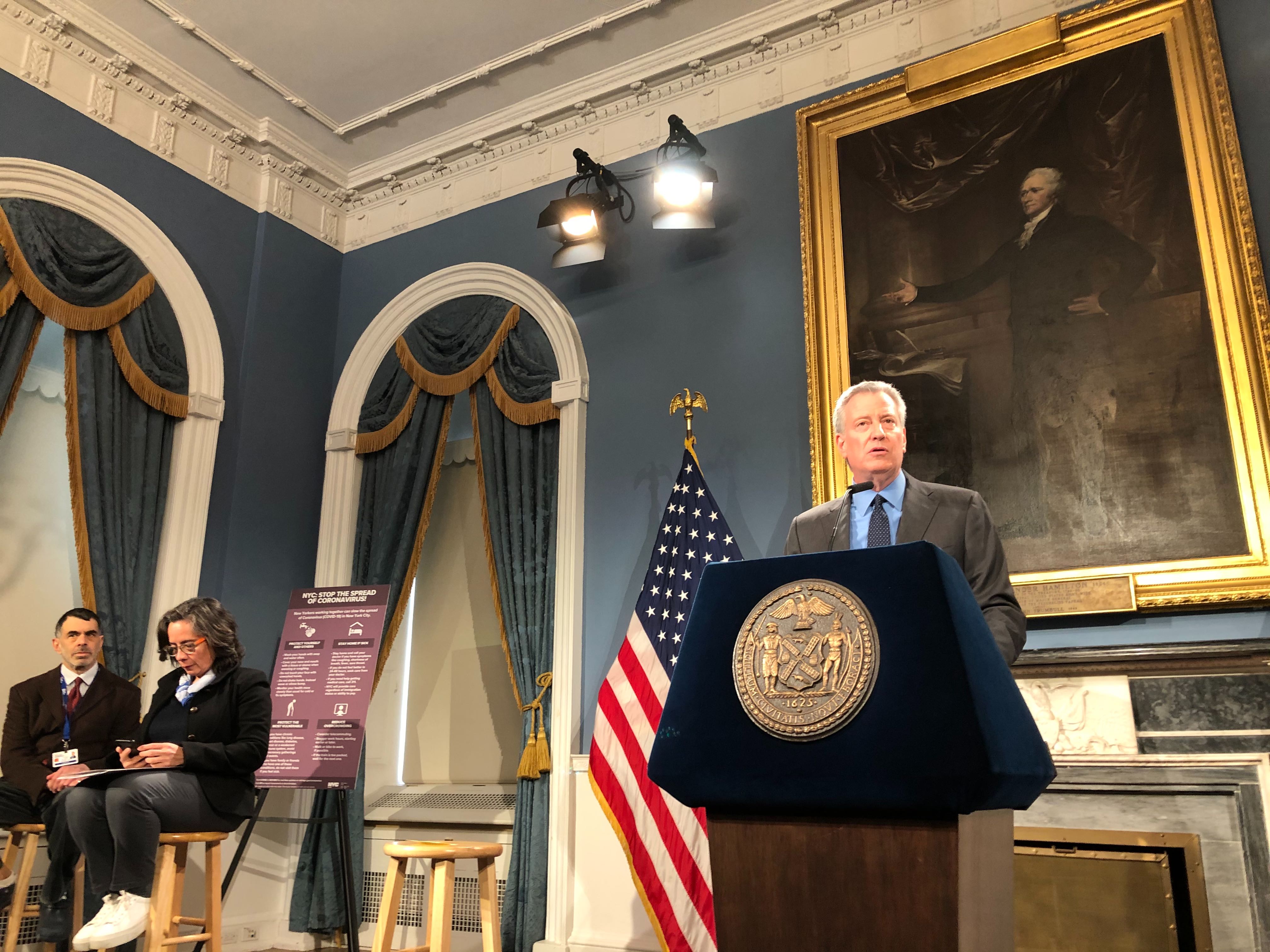 Mayor de Blasio stands behind a lectern during a Saturday, March 14, 2020 press conference about coronavirus. Health Commissioner Barbot sits behind him.