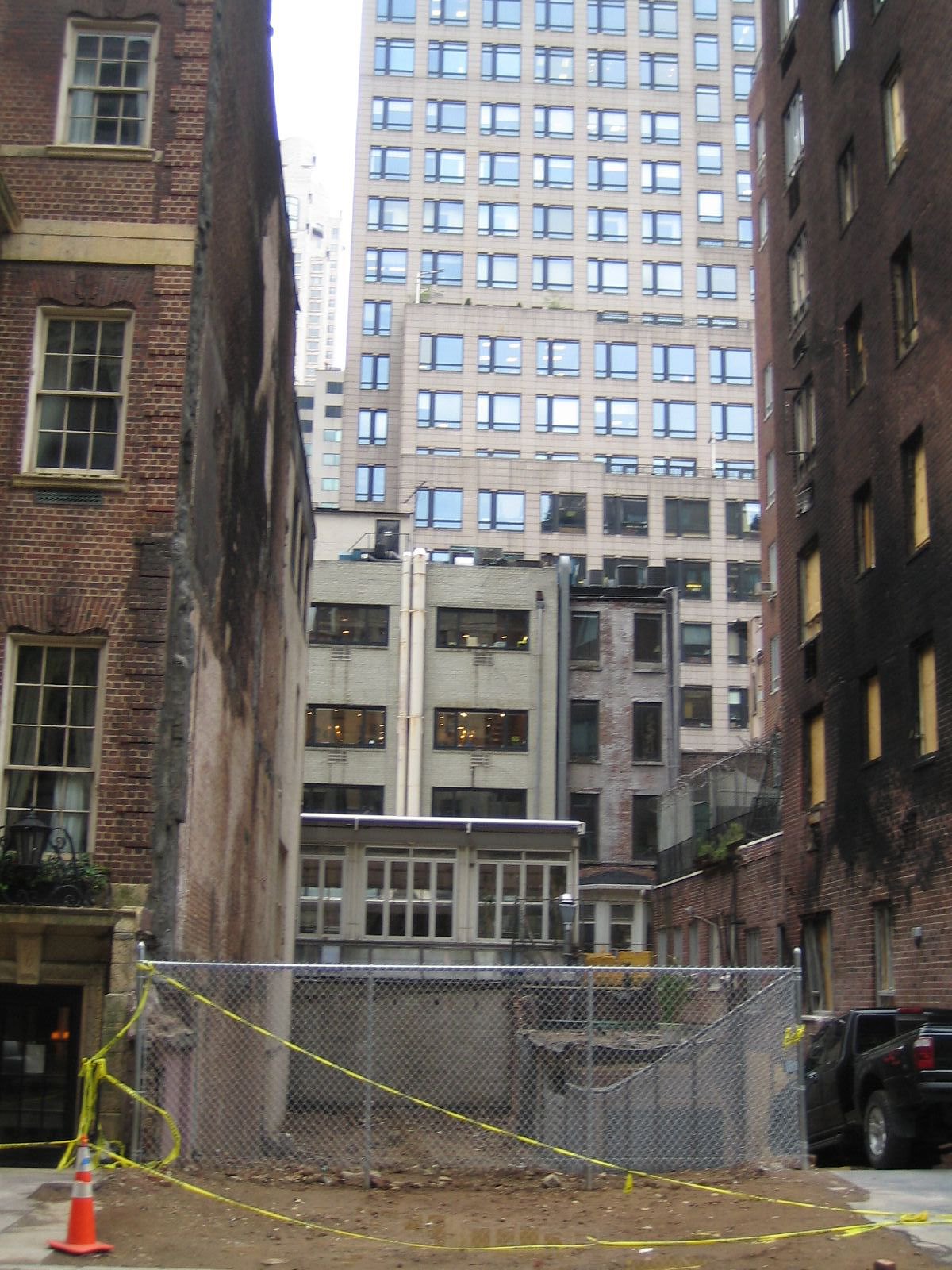 The vacant lot at 34 East 64th Street, with a chain link fence in front. Black smoke from the explosion is still visible on nearby buildings.