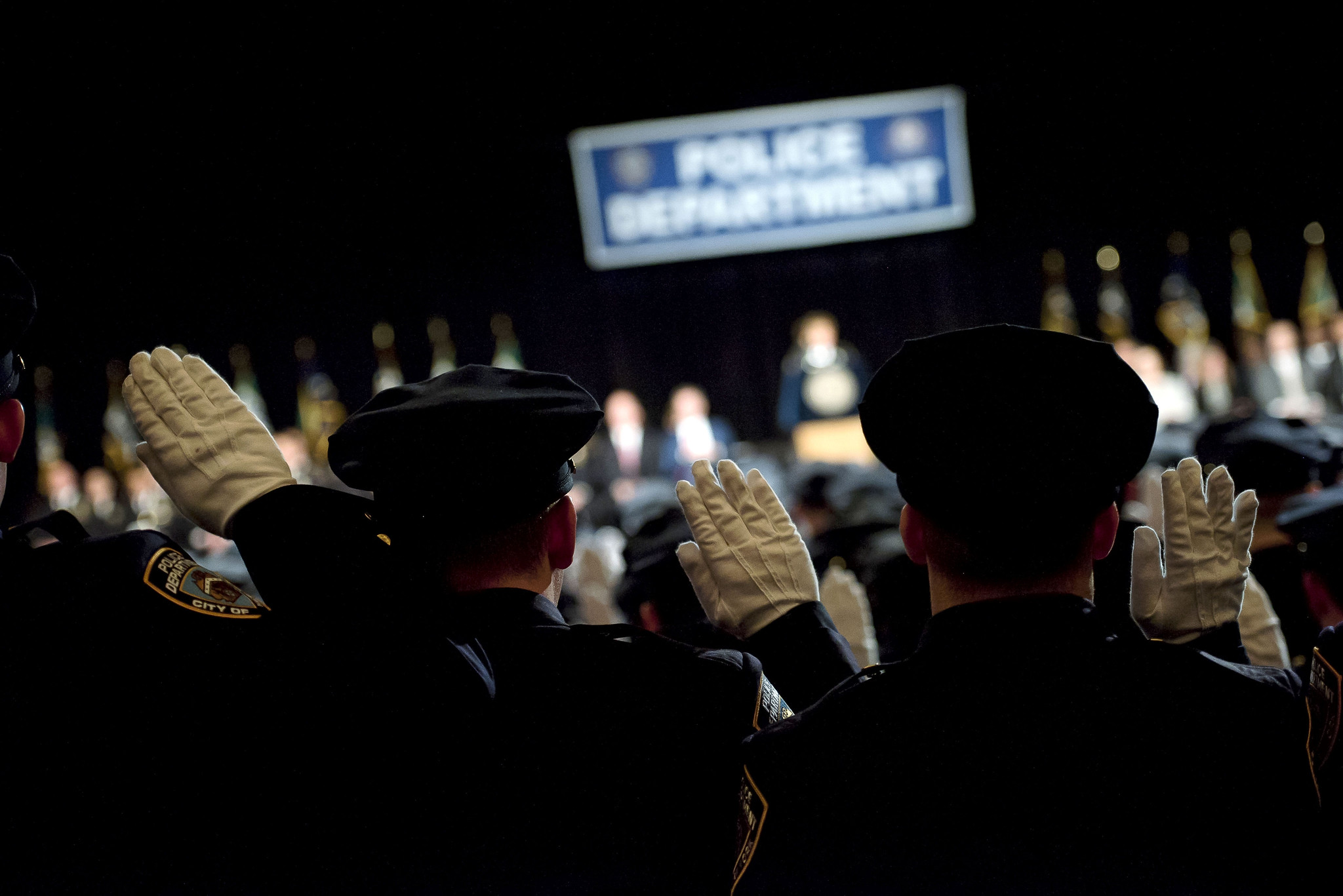 Silhouette of NYPD cadets graduating, with a sign in the background that says "NYPD Graduation"