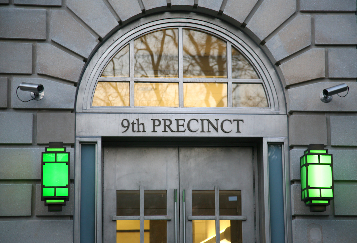 Green lanterns flank the entrance to the grey 9th precinct in Manhattan