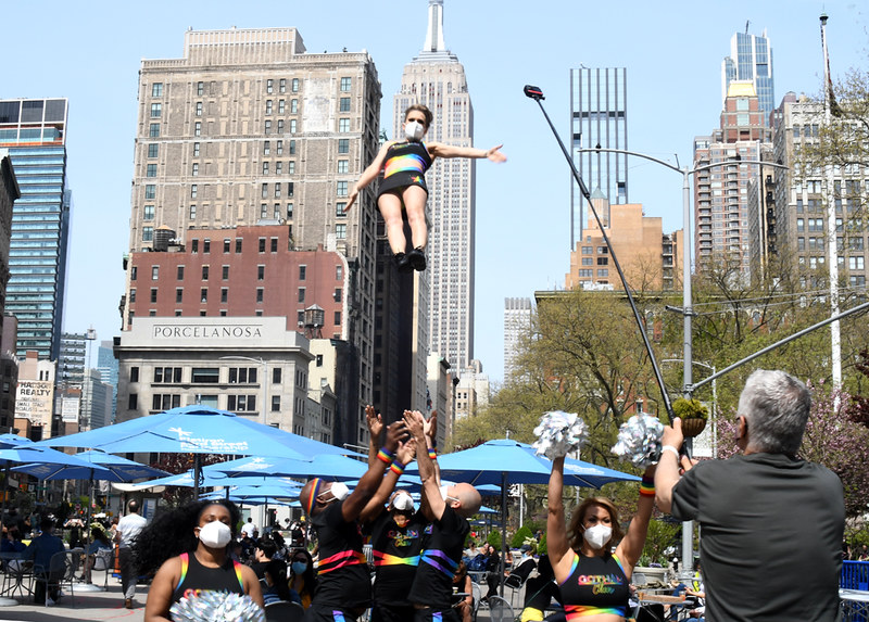 A cheerleader floats in mid air above her teammates who prepare to catch her in Madison Square Park.