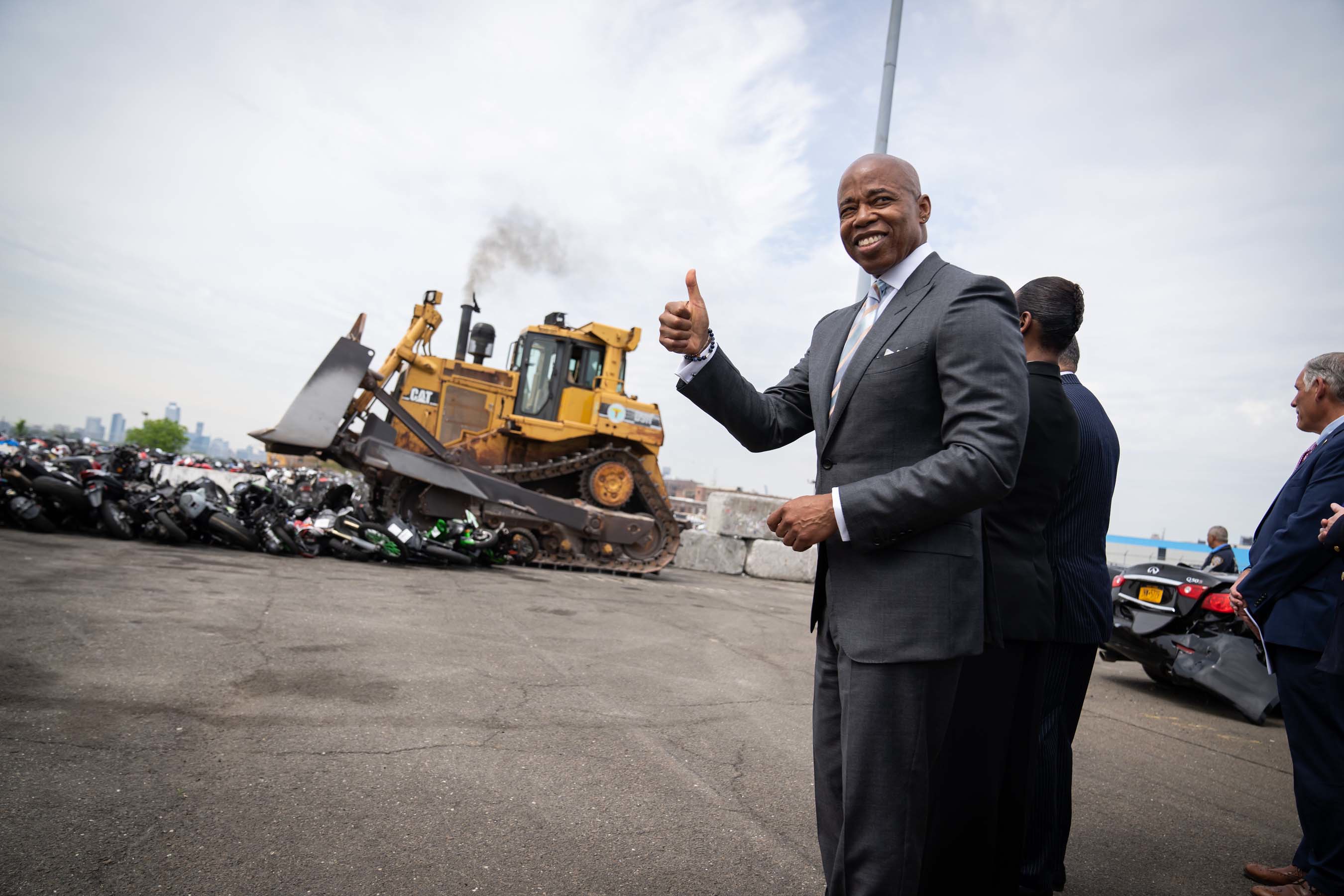 Eric Adams stands in front of bulldozer crushing dirt bikes
