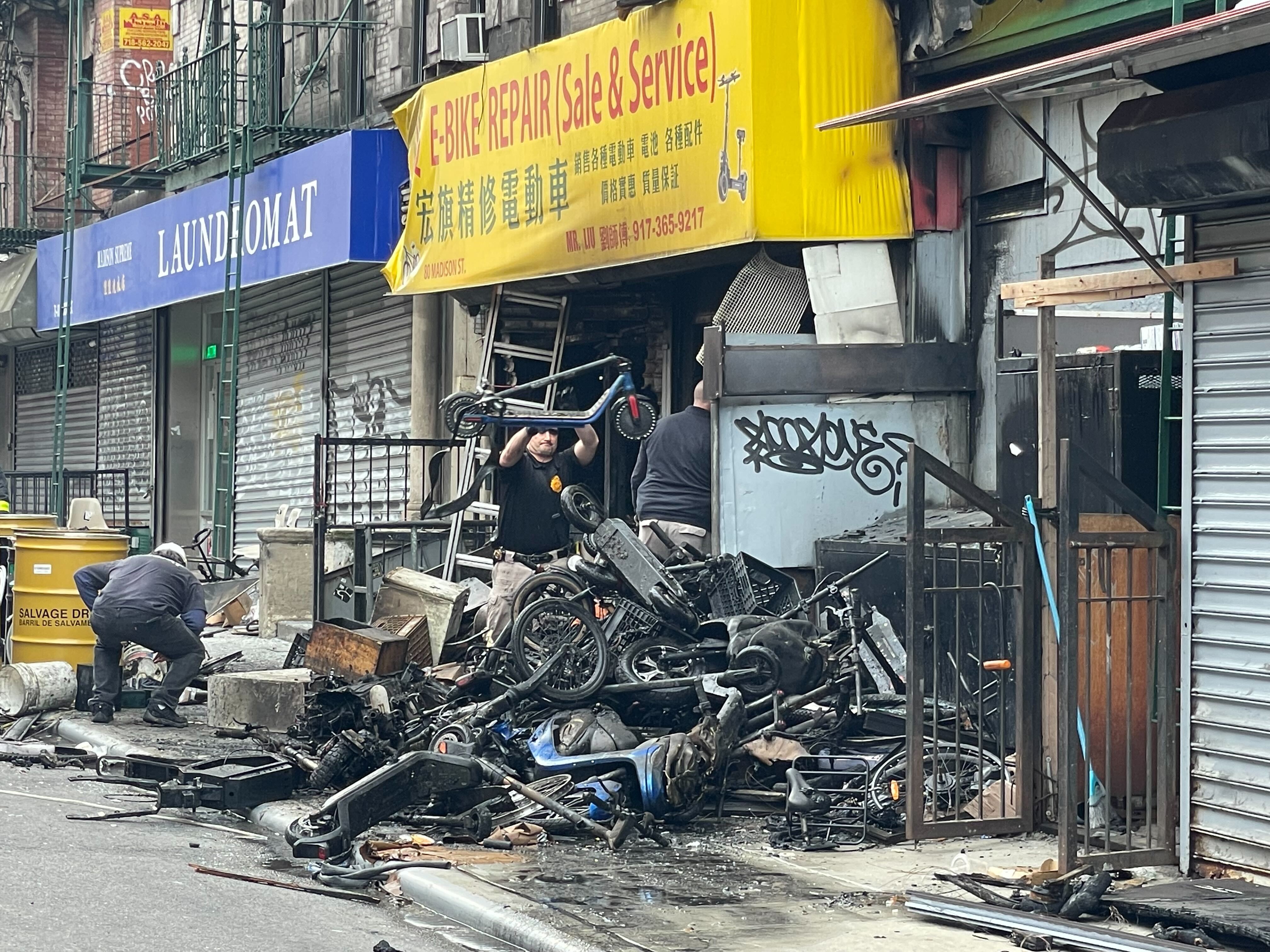 A photo of emergency workers sorting through the wreckage after a fire at an e-bike shop in Chinatown killed at least 4 people.