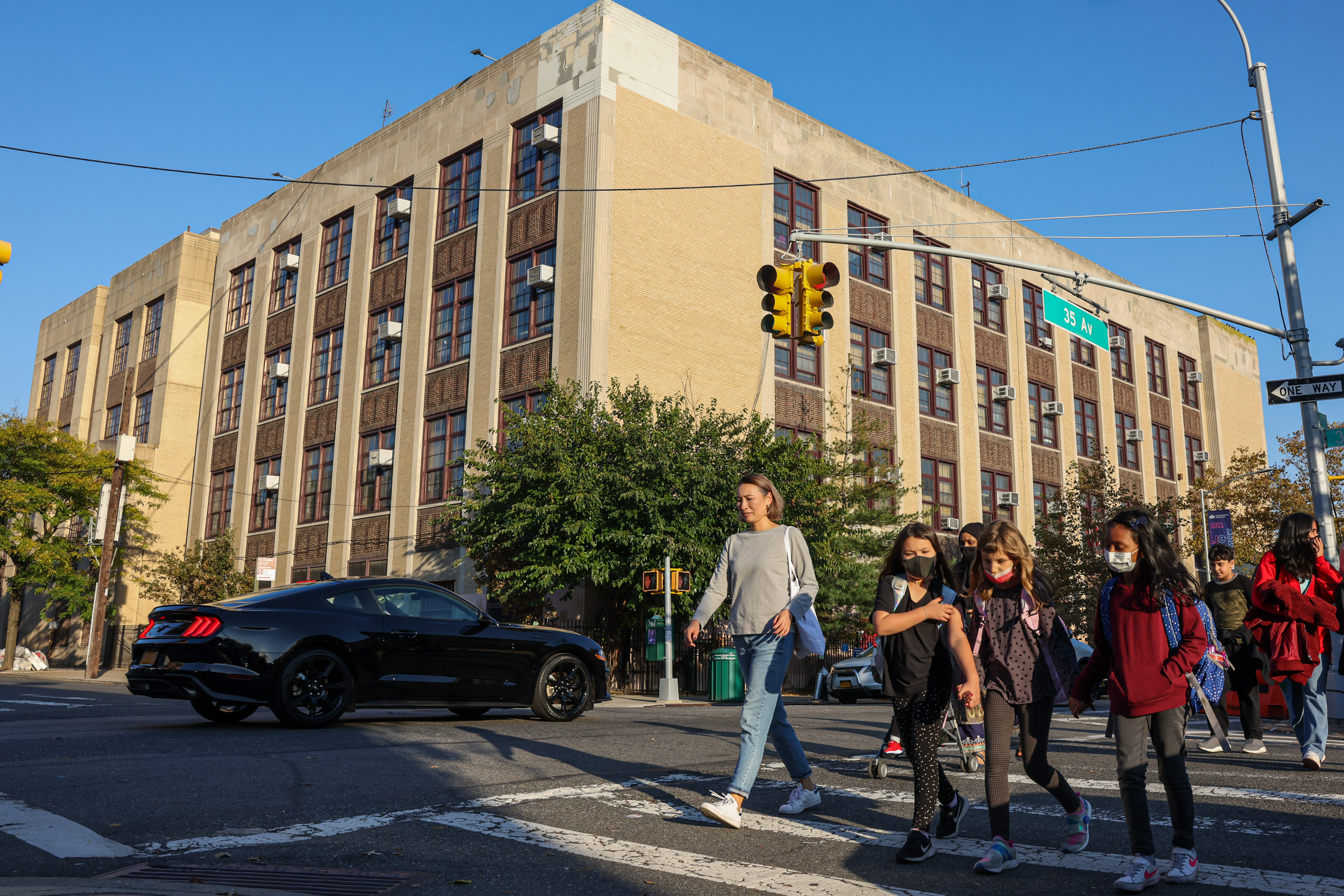 exterior of PS 166 in Queens, seeing the building from across the street with children crossing the street in the foreground