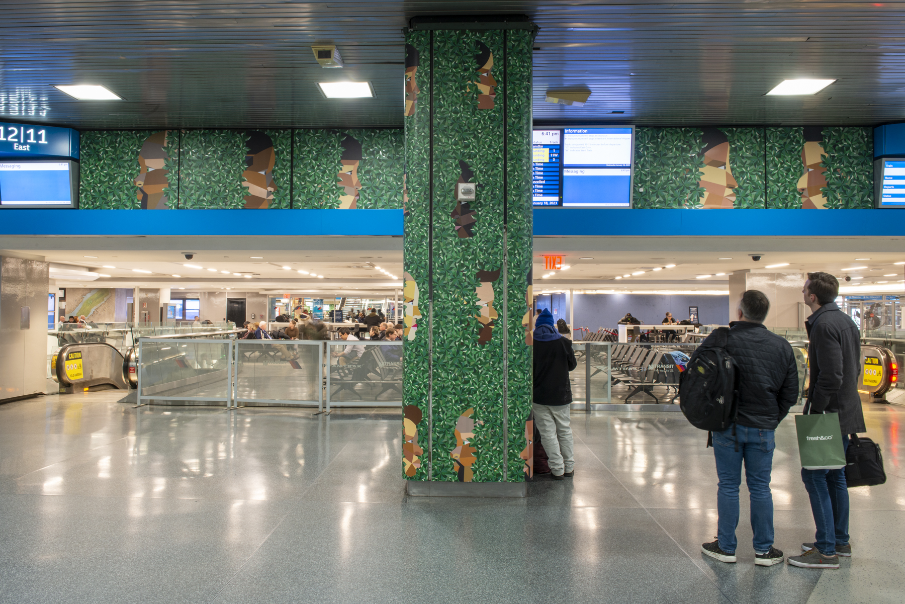 A train station concourse adorned with green, leafy art.