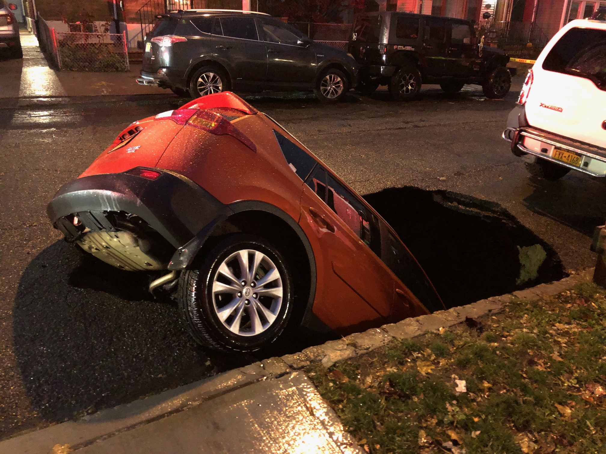 An orange vehicle is submerged in a sinkhole at a residential street in Queens on Thanksgiving.