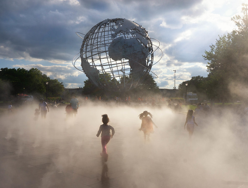 A group of young kids run through mist at the globe fountain in Flushing Meadows Corona park.