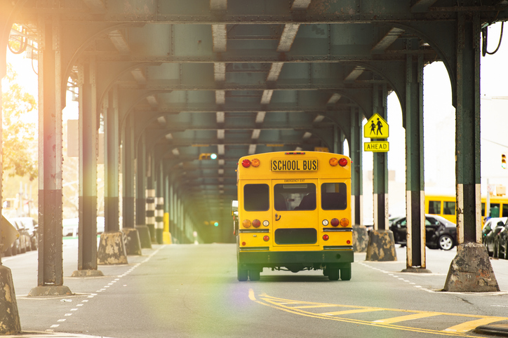 a school bus traveling on a road, under an overpass