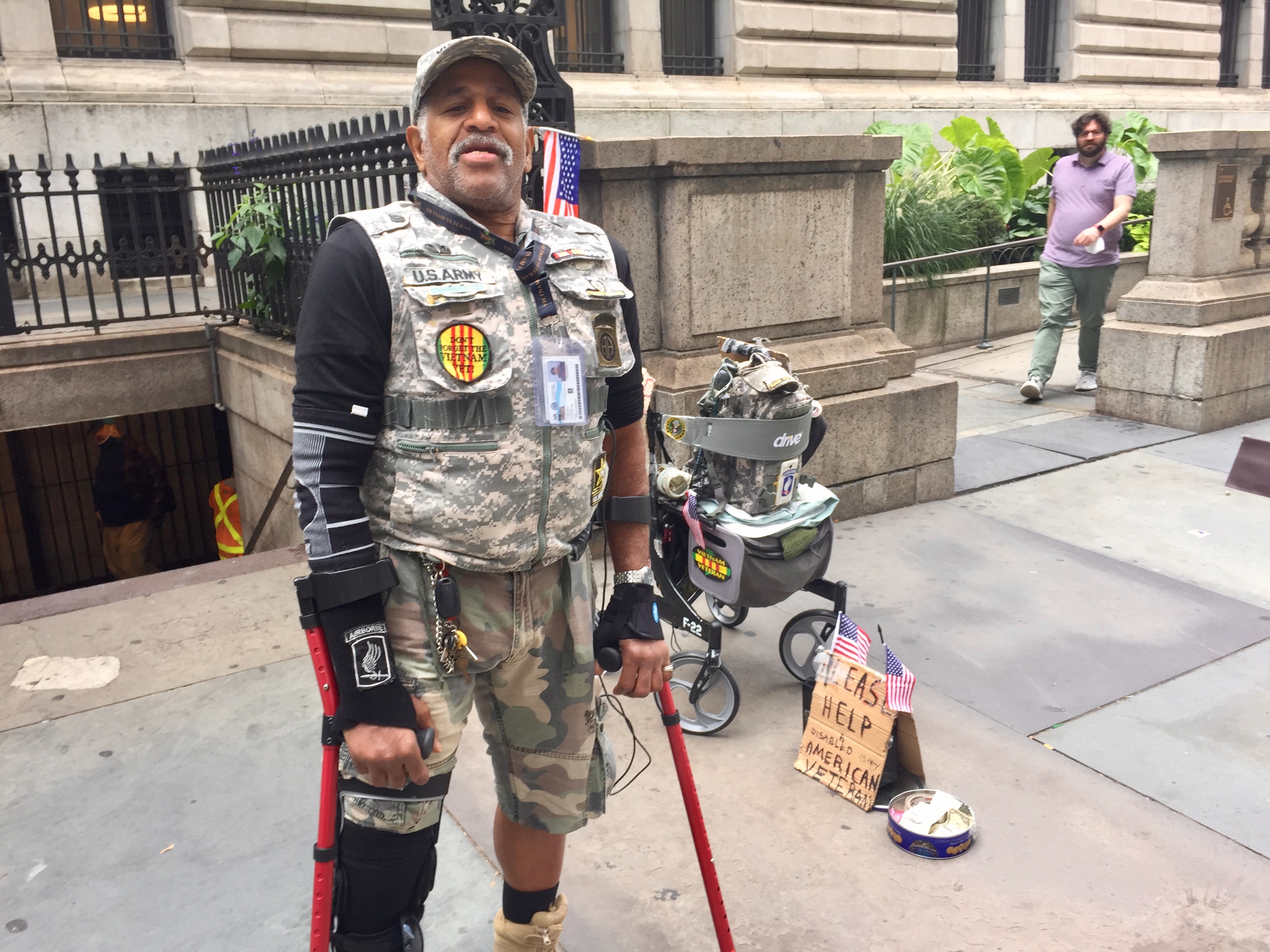 A man wearing a flak jacket and shorts, using crutches