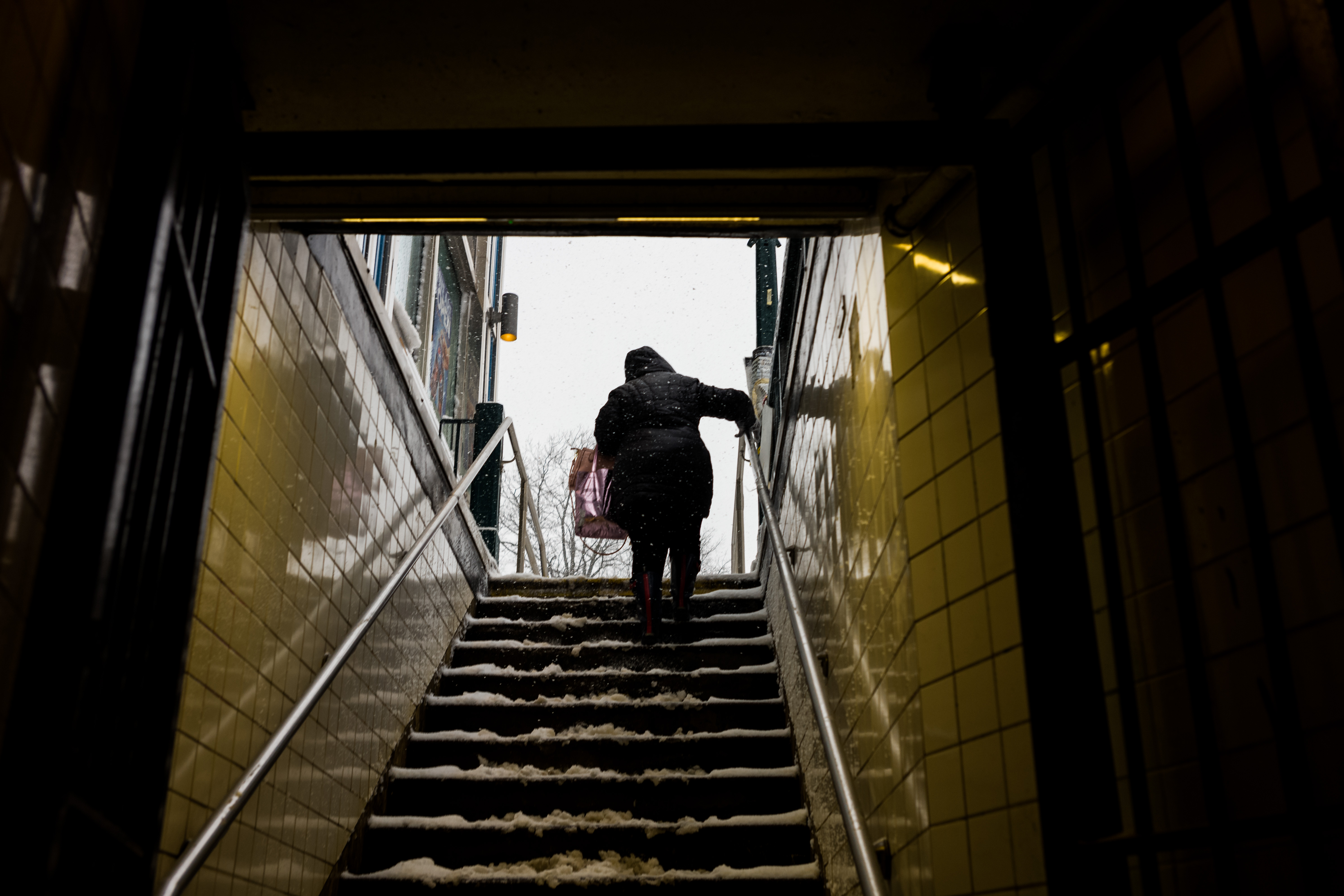 A woman walks up subway stairs to the sidewalk