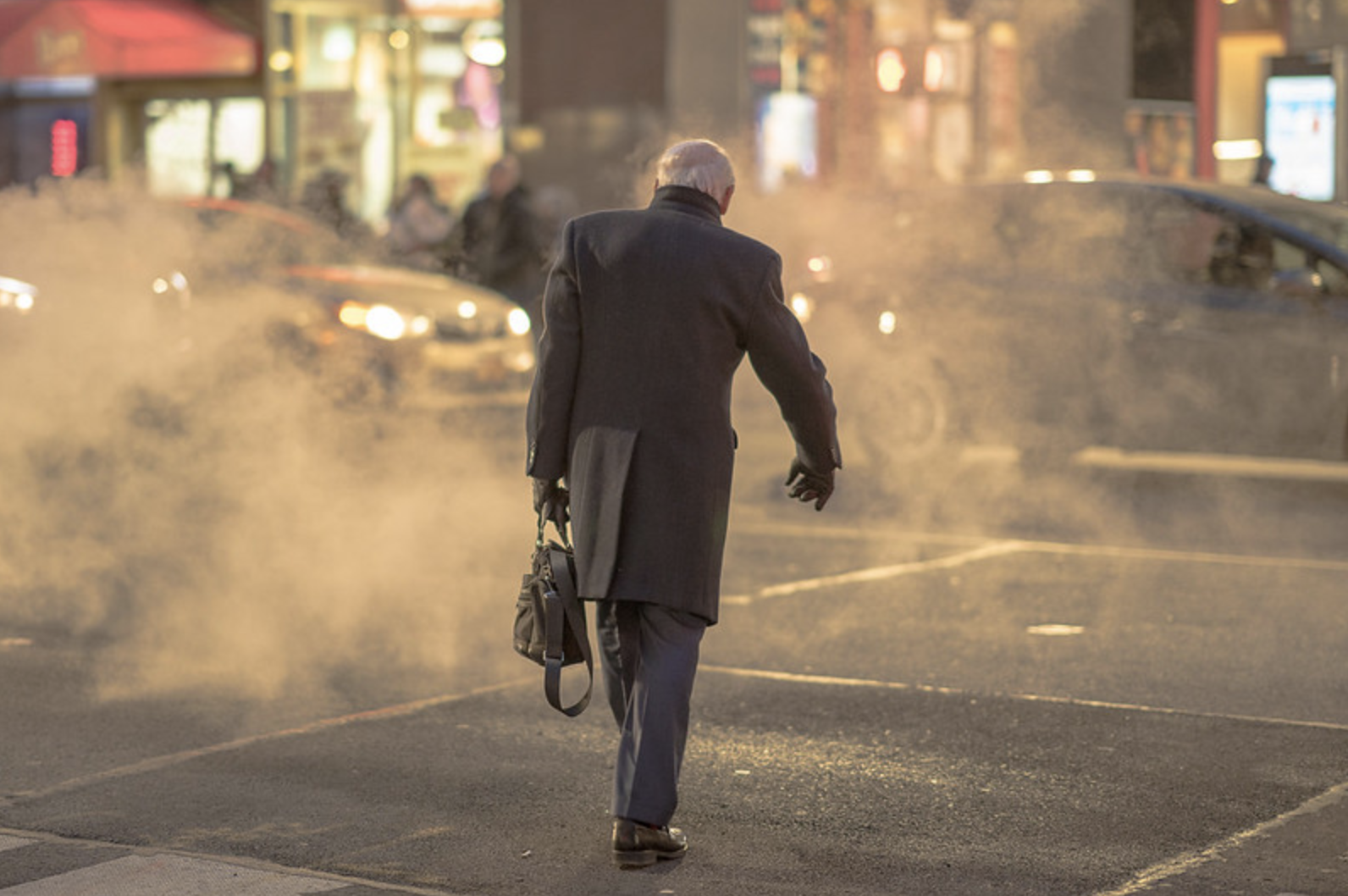 A man wearing an overcoat and gloves is seen walking from behind in Manhattan.