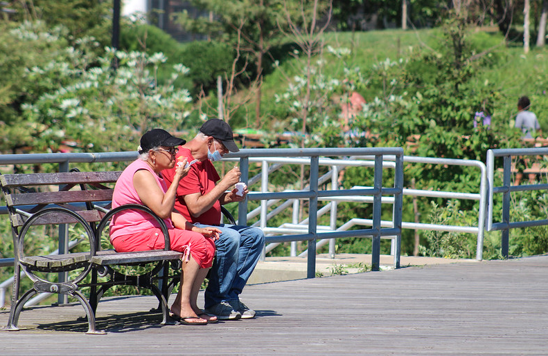 two seniors sit on a park bench eating ice cream