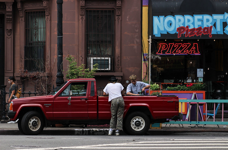a red pickup truck in front of a pizzeria