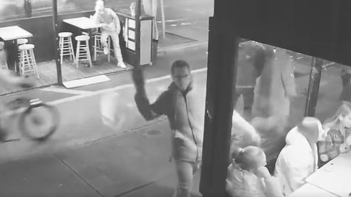 A still of surveillance footage showing a suspect hurling a brick at the bar window.