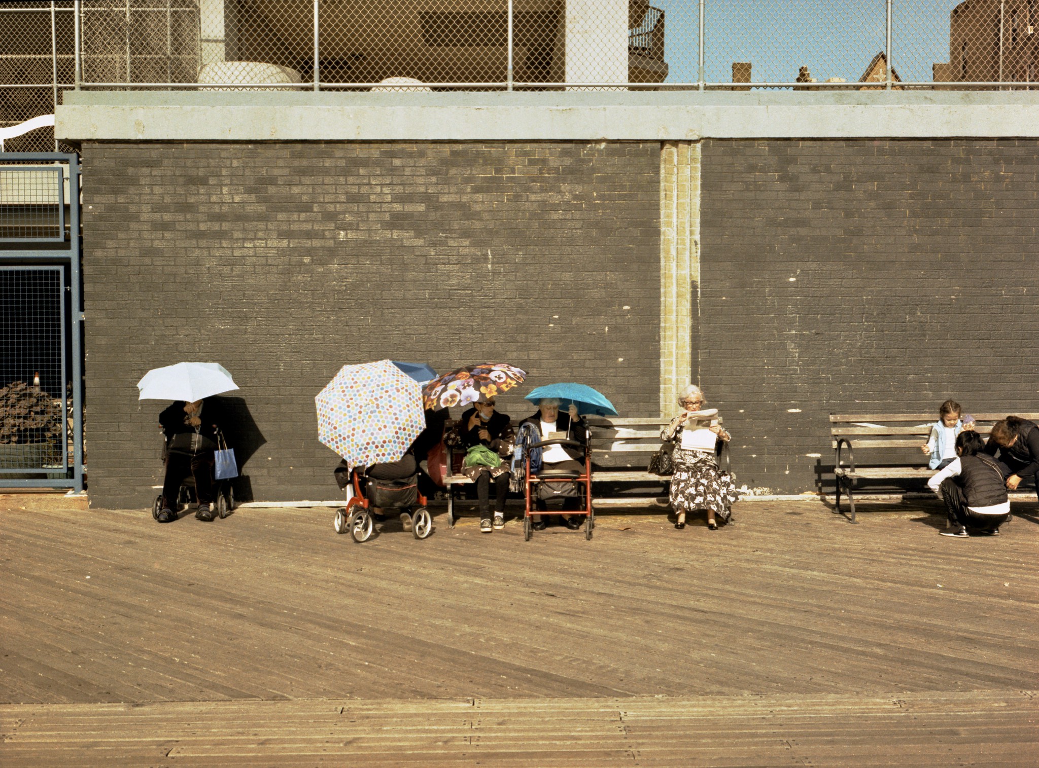 people with umbrellas sit on the Brighton Beach boardwalk