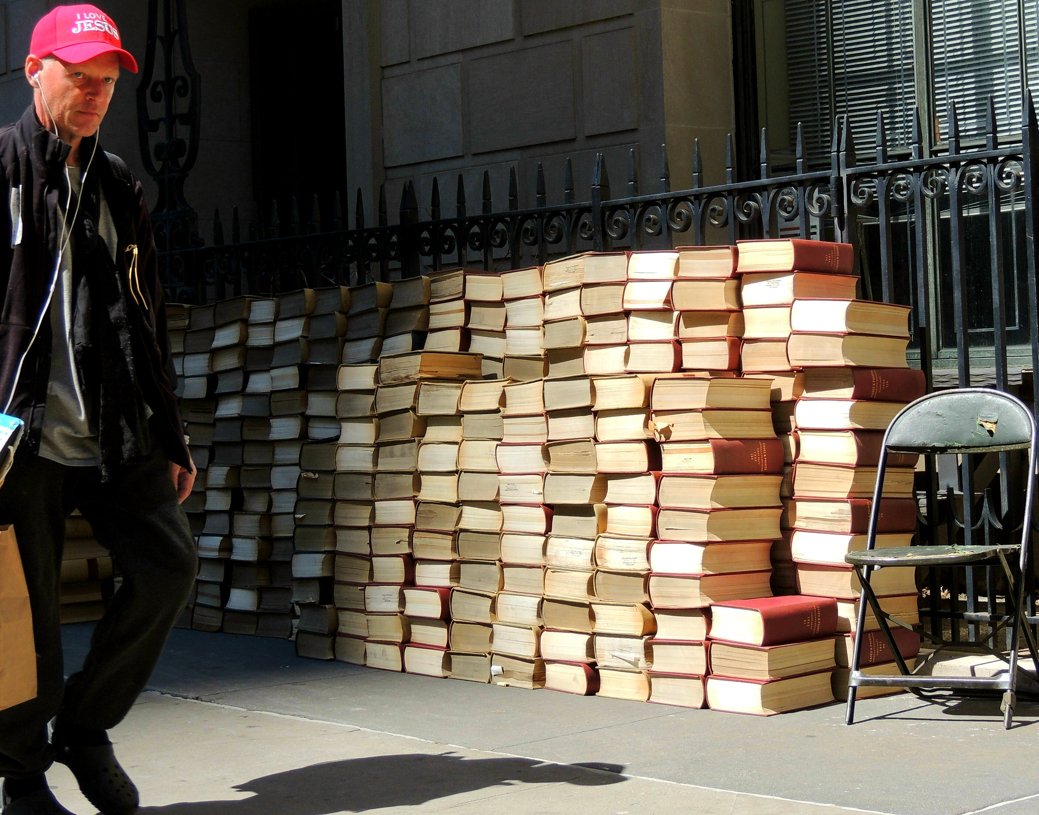 a guy walks by a bunch of stacked books on a Brooklyn sidewalk