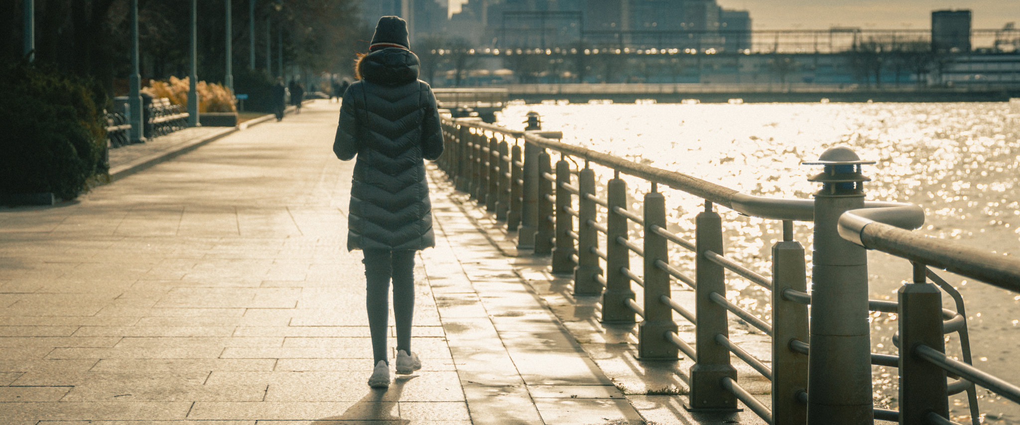 a woman walks by the Hudson River on a cold day