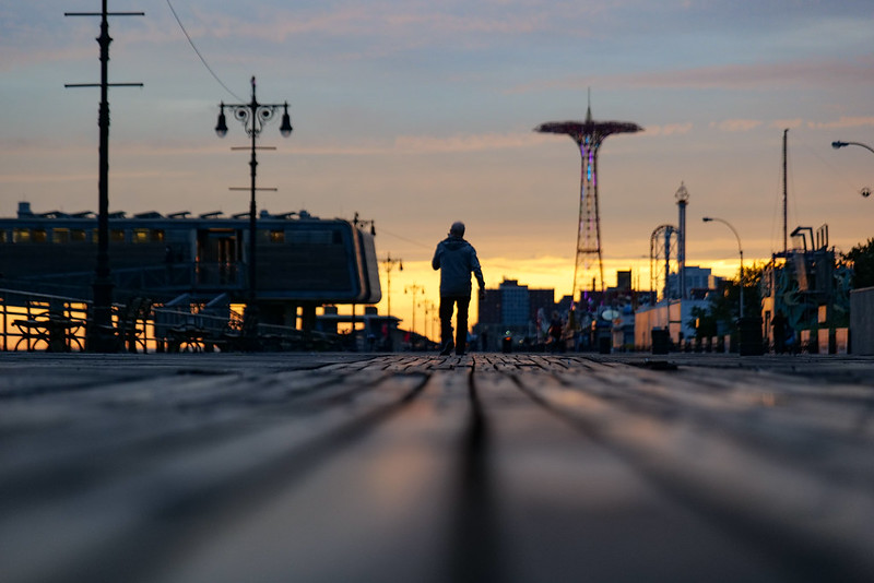 a man walks on the Coney Island boardwalk at sunrise