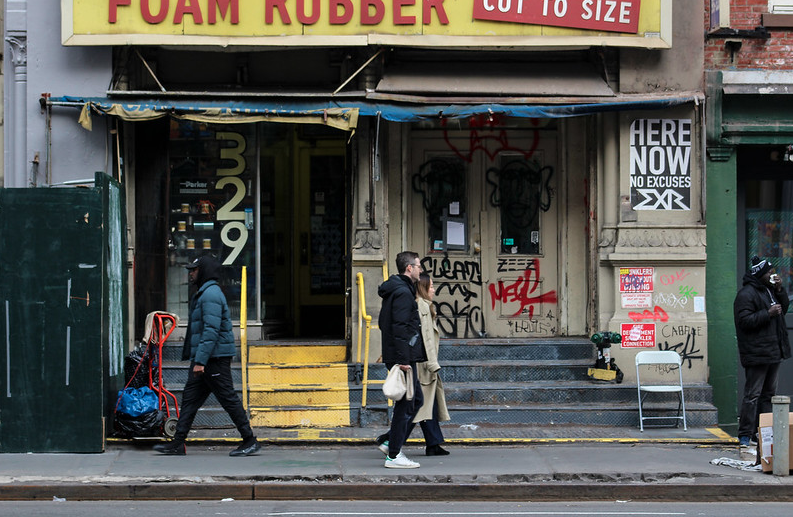 a few people walk down Canal Street in front of a foam rubber shop