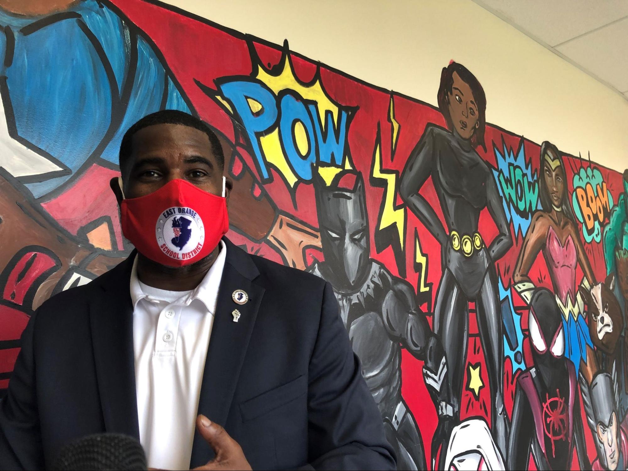 Photograph of East Orange Superintendent AbdulSaleem Hasan wearing a mask in front of a colorful mural