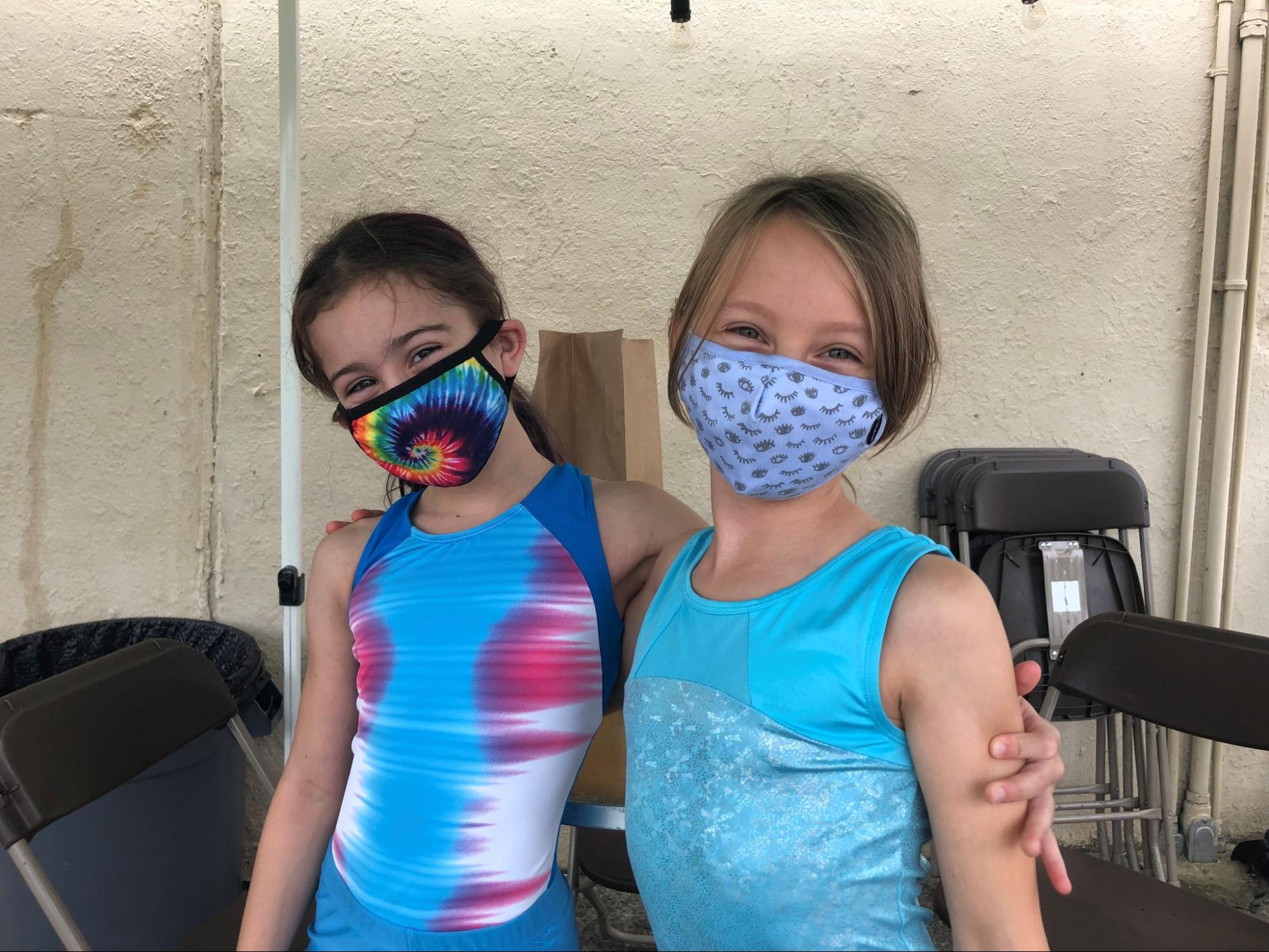 Two young girls wearing masks, with their arms around their shoulders