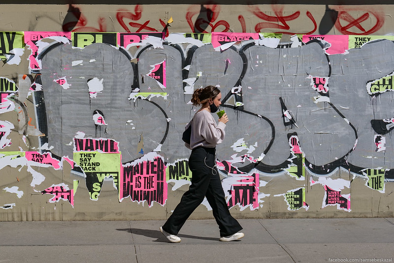 a woman walks past a colorful wall of posters and tagging