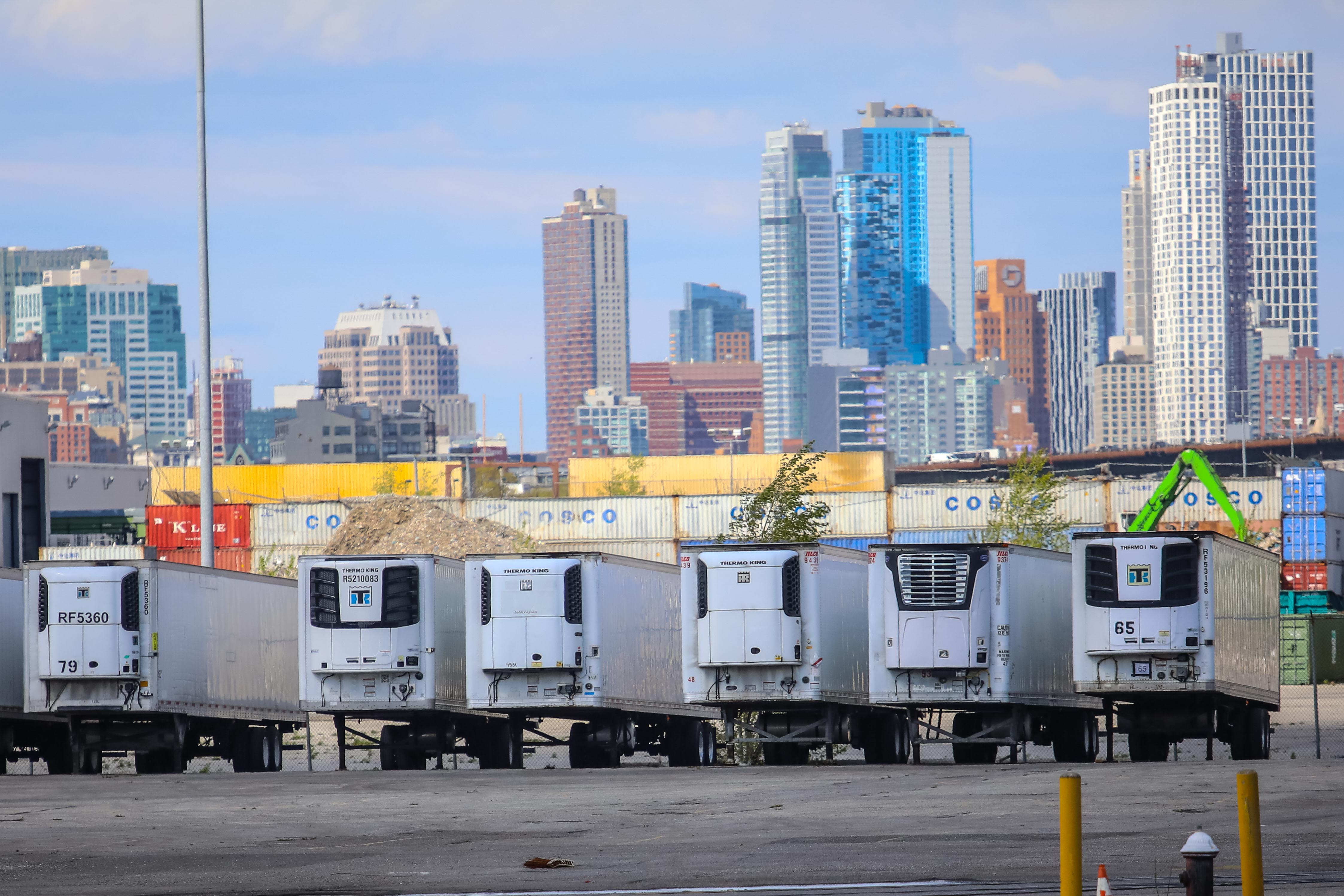 Dozens of freezer trucks on the pier, with the lower Manhattan skyline in the distance