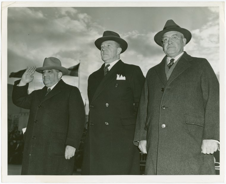 Fiorello Laguardia saluting in a black and white photo with two other men in overcoats