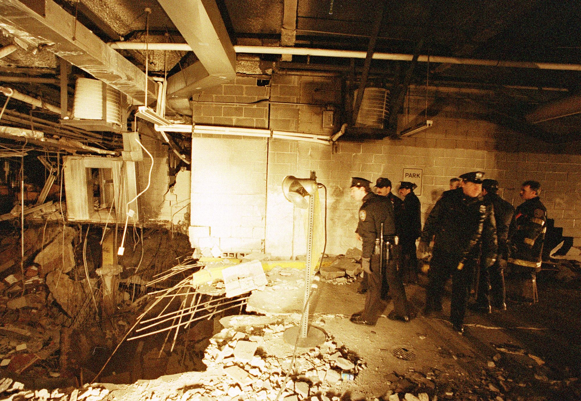 POlice officers and firefighters look at a huge crater in the parking garage