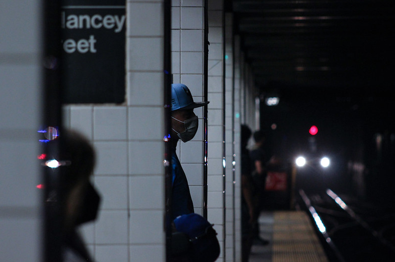 someone in a face mask waits for a subway at Delancey St