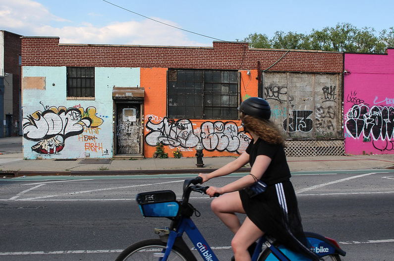 a person on a Citi Bike rides past some graffiti'd buildings