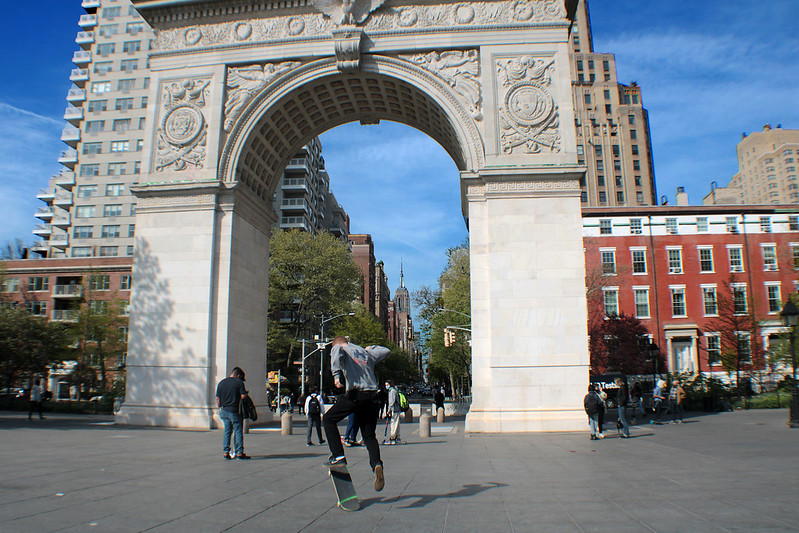 a man on a skateboard ollies in front of the arch at Washington Square Park