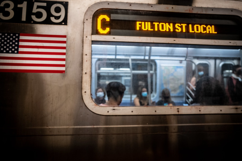 A photo of masked riders inside a C train car that's Fulton Street-bound.